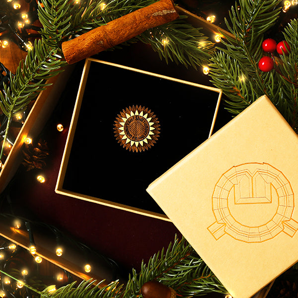 Decorative brooch in a box with Christmas elements like pine branches and lights.