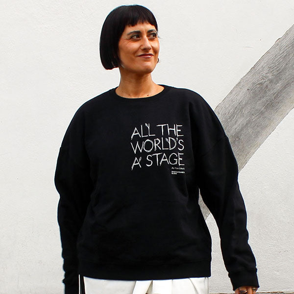 Person wearing a black sweatshirt with text, standing against a light gray wall.