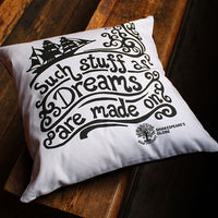 White pillow with black text and ship design on a wooden surface, featuring Shakespeare's Globe.