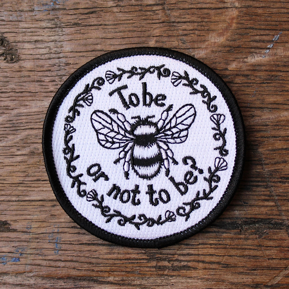 
                  
                    White circular sew on patch with black border and black graphic text and embroidered bee
                  
                