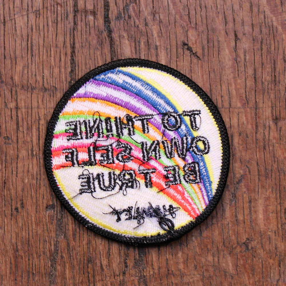 
                  
                    Rainbow yellow patch with black border and bold black text, circular shape, reverse side
                  
                