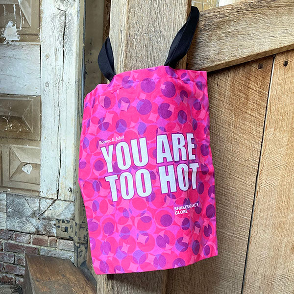Pink bag with text 'YOU ARE TOO HOT' hanging on a wooden post