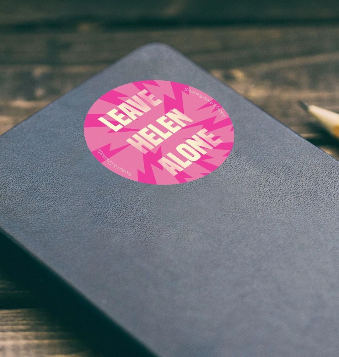 Pink sticker with 'Leave Helen Alone' text on a black notebook
