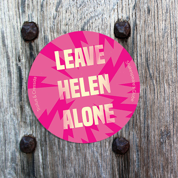 Pink circular sticker with 'Leave Helen Alone' text on a wooden background