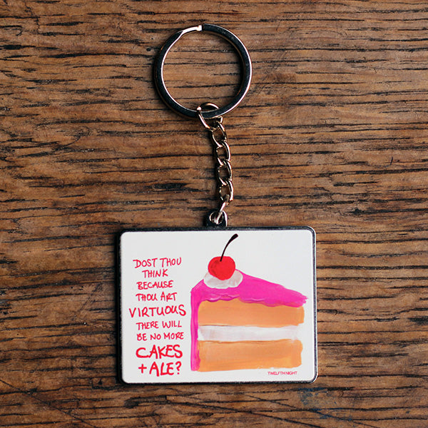 Silver coloured metal keyring with flat portrait orientated image of a slice of cake with scratchy pink graphic text on a white background