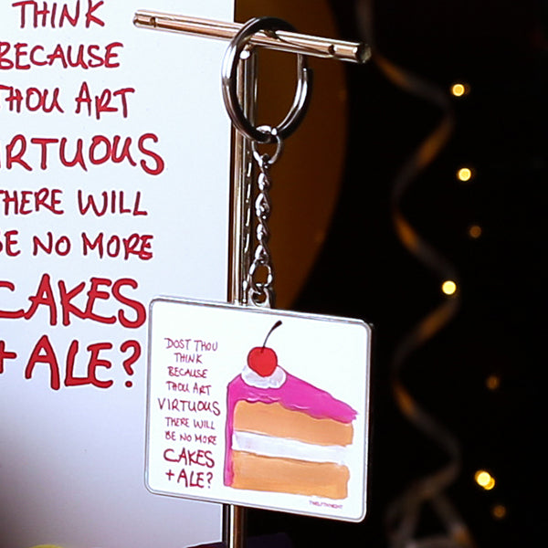 Silver coloured metal keyring with flat portrait orientated image of a slice of cake with scratchy pink graphic text on a white background