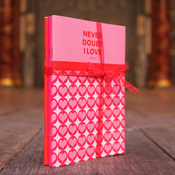 Paperback small notebook in pinks, reds, and white, with graphic text and hearts