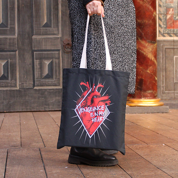 
                  
                    Black cotton bag with natural cotton handles, printed with an image celebrating Shakespeare play, Titus Andronicus. A red anatomical heart is partly enclosed by a white diamond frame. Gold rays emanate from behind the frame. Across the front of the image is a quote from the play (vengeance is in my heart) in white lettering.
                  
                