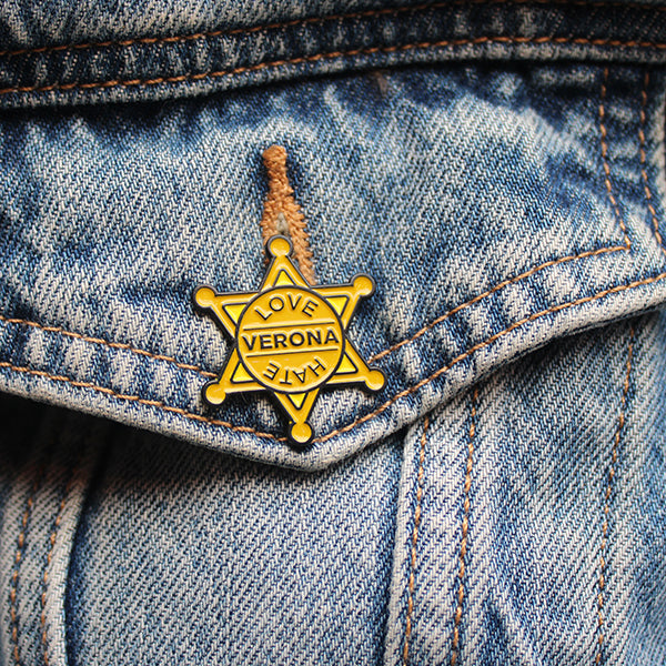 Yellow sheriffs badge with black outline and black text, pinned onto denim