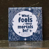 Square blue magnet featuring the quote "What fools these mortals be!" from A Midsummer Night's Dream in bold white lettering, surrounded by illustrated leaves, stars, and mushrooms.