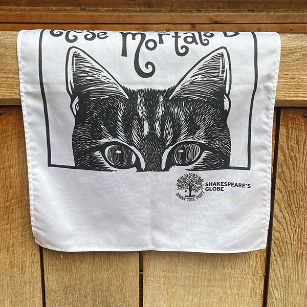 White tea towel with black cat illustration and 'Shakespeare's Globe' logo on a wooden surface