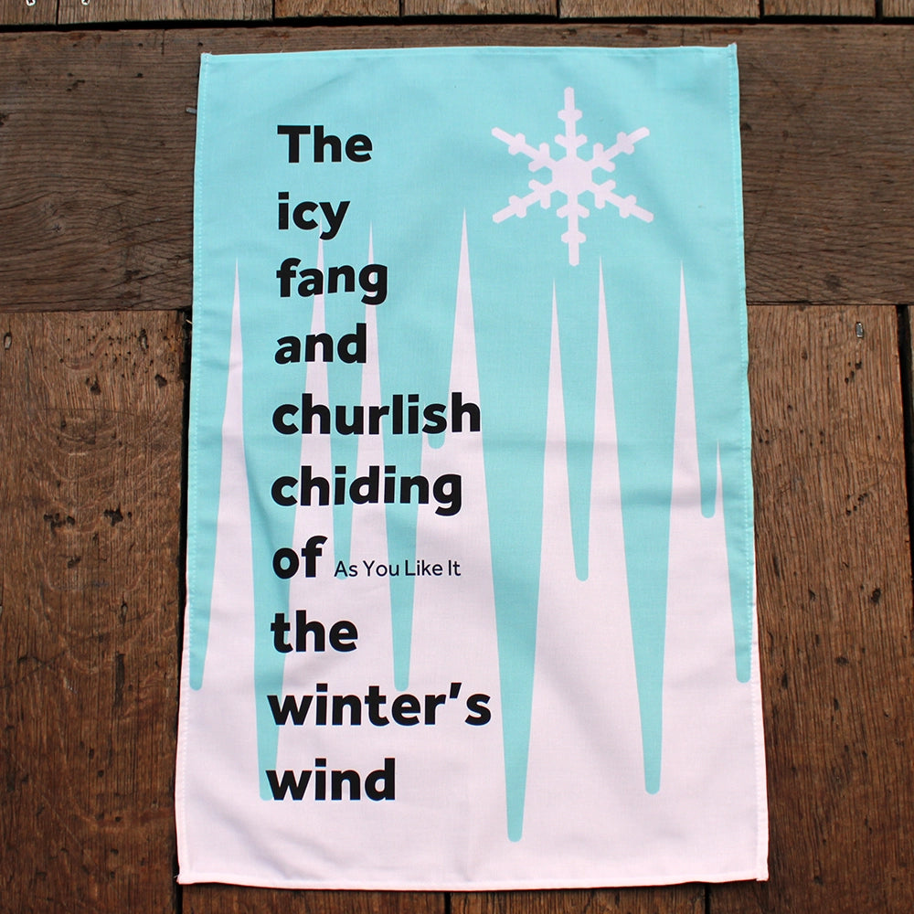 White tea towel with an icicle pattern in cold blue, white snowflake, and a quote in black 