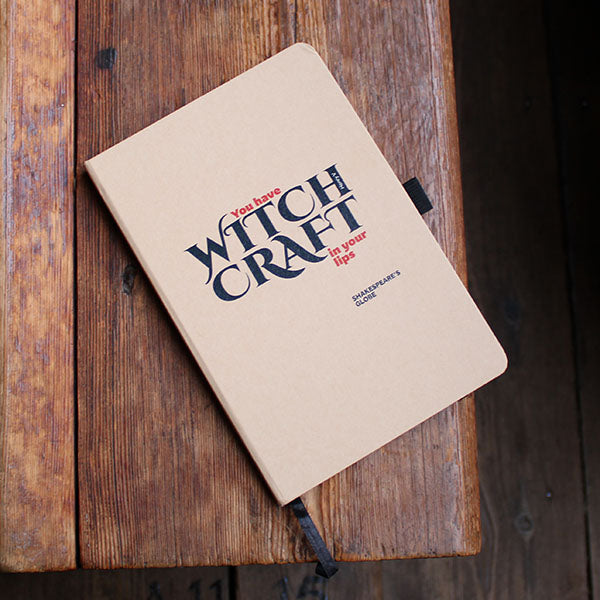 Notebook with 'You have WITCH CRAFT in your lips' text on a wooden surface