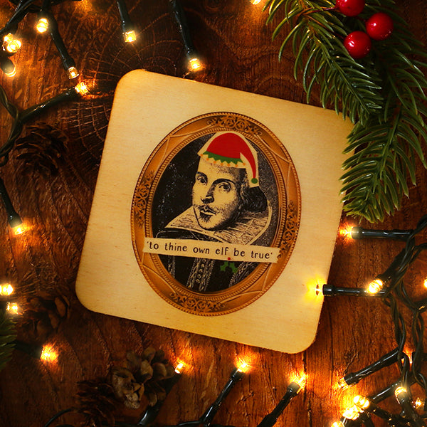 Decorative wooden coaster with a printed design of Shakespeare wearing a Santa hat, surrounded by Christmas lights and decorations.