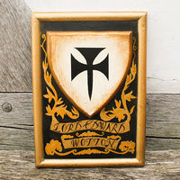 Wooden shield with black and gold design on a wooden surface