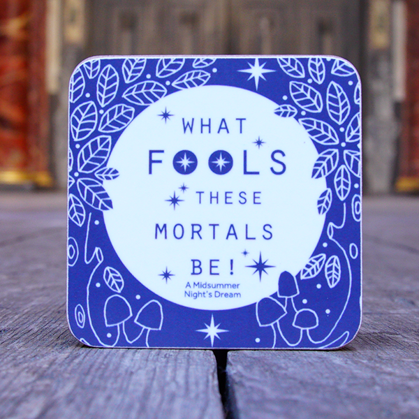 Square melamine coaster with an image celebrating Shakespeare play,  Midsummer Night's Dream. The Image consists of a white circle on a royal blue ground, representing a full moon in the night sky. Surrounding the 'moon' are hand-drawn leaves and berries and a tree trunk either side. Across the face of the 'moon' is a quote from the play in narrow san serif capital letters (what fools these mortals be!)