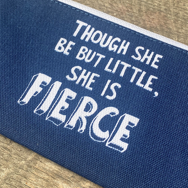A mid-blue cotton pencil case with a white zip. The pencil case is printed on both sides with a quote from Shakespeare play, A Midsummer Night's Dream (though she is but little, she is fierce) in white hand-drawn capital letters.