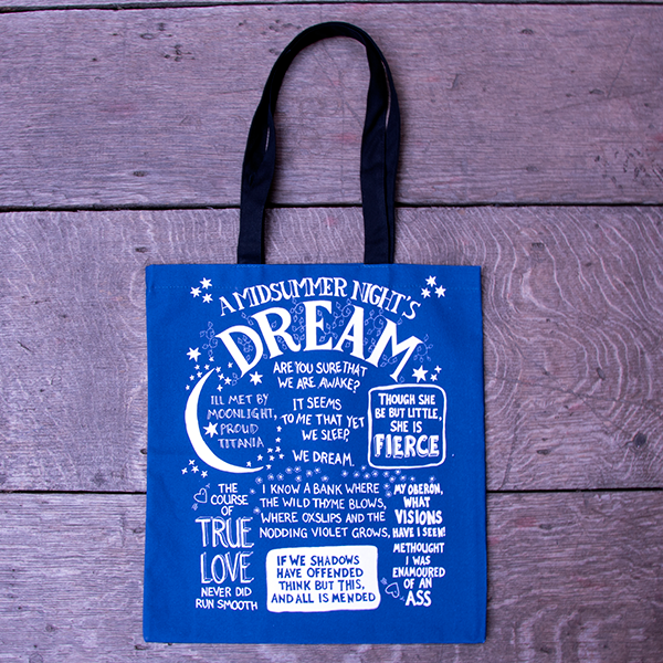 Mid-blue cotton bag with black mid-length handles. The bag is covered in well-known quotes from Shakespeare play, A Midsummer Night's Dream printed in white. Each quote is rendered in hand-drawn lettering, each in a slightly different style - all in capital letters. The name of the play is a the top of the design and is surrounded by hand-drawn leaves. The quotes are surrounded by hand-drawn stars, flowers and a crescent moon all also printed in white.