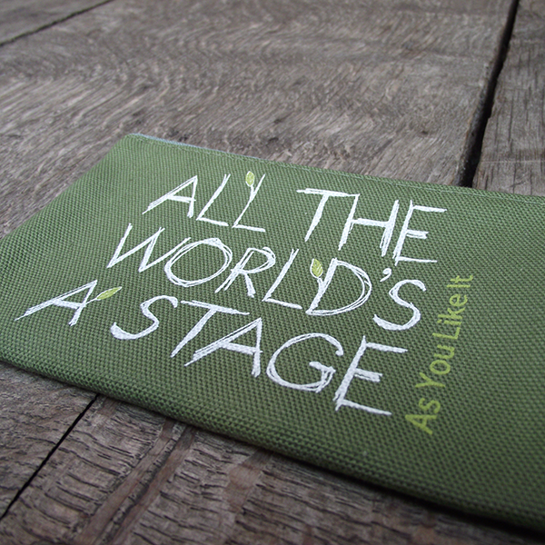 
                  
                    Sage green cotton zipped purse with a quote from Shakespeare play, As You Like It (all the world's a stage) printed in white. The lettering is hand-drawn in a scribbled style and several of the letters have little lime green leaves 'growing' from them. The title of the play is printed in lime green up the right hand side of the quote.
                  
                