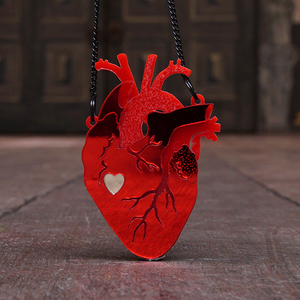 
                  
                    Pendant in the shape of an anatomical heart. The pendant is made of bright red Perspex in several layers, giving the appearance of three dimensions. The top layer has channels cut to represent veins and the under layers are textured. A cutout in the shape of a graphic heart sits about halfway down the pendant and is filled in with silver Perspex. The pendant is on a black chain.
                  
                
