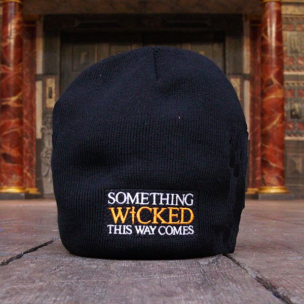 
                      
                        Black beanie hat with an embroidered quote on the front from Shakespeare play, Macbeth, "something wicked this way comes." The quote is in white capital letters with the word 'wicked' in bright orange capital letters.
                      
                    