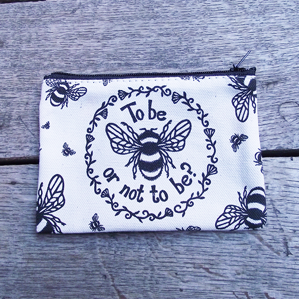 Rectangular purse made from unbleached cotton with a black zip closure. The purse is printed with a design adapted from an original print in black, a bumble bee and a quote from Shakespeare play, Hamlet (to be or not to be) is surrounded by a ring of flowers and leaves. Smaller bees surround the central image, flying in different directions.
