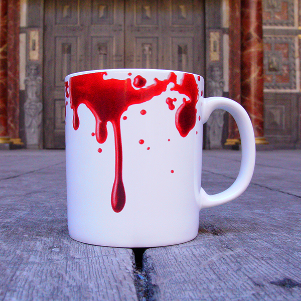 White earthenware coffee mug with a design of realistic red blood drips circling the rim and dripping down the mug. Inside the inner rim of the mug is a quote from Shakespeare play, Macbeth (Out, damned spot! Out, I say!) written in angry hand-drawn black letters. The O in the word spot is represented by a single drop of red blood.