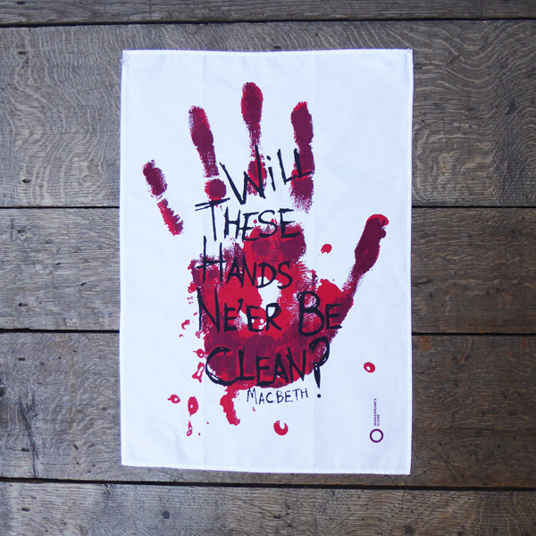 White cotton tea towel printed with a large bloody hand-print in reds. Over the hand-print, printed in black is a quote from Shakespeare play, Macbeth (Will these hands ne'er be clean?) The lettering is in an angry, hand-drawn style.