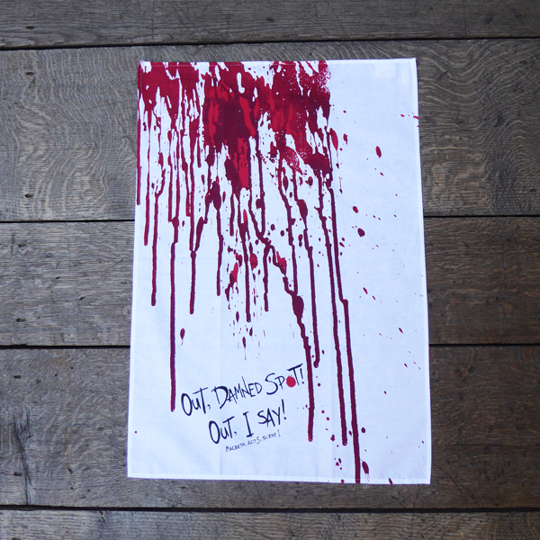 White cotton tea towel with a print of blood dripping down the length of the towel, in reds. At the bottom of the towel is a quote from Shakespeare play, Macbeth (Out. damned spot! Out, I say!) The quote is written in an angry hand-drawn style in black.