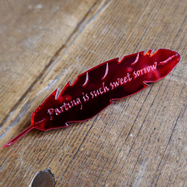 Red mirrored acrylic brooch shaped like a quill and engraved with a quote from Romeo and Juliet