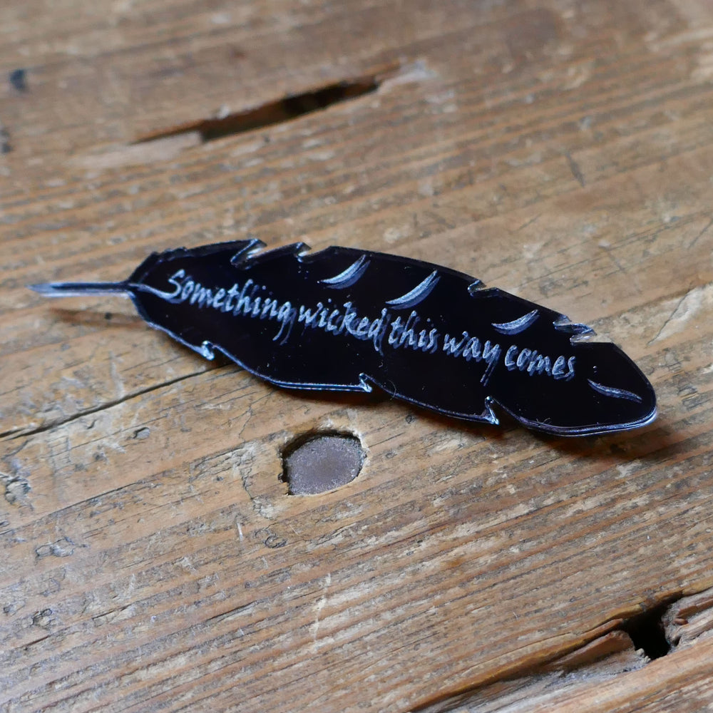 Black, mirrored acrylic brooch in the shape of a quill, engraved with a quote from Shakespeare play, Macbeth, "something wicked this way comes".