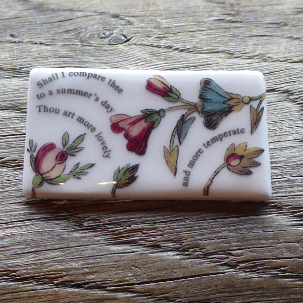 
                  
                    Rectangular ceramic brooch with lines from Shakespeare's Sonnet 18 and images of flowers
                  
                