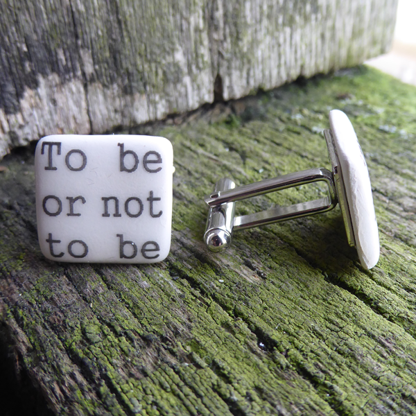 
                  
                    Square ceramic cufflinks made of creamy white glazed earthenware. Each cufflink has part of a quote from Shakespeare play, Hamlet in black in a simple serif font. One cufflink says "To be or not to be" and the other "That is the Question". The cufflinks have silver-plated fixings
                  
                