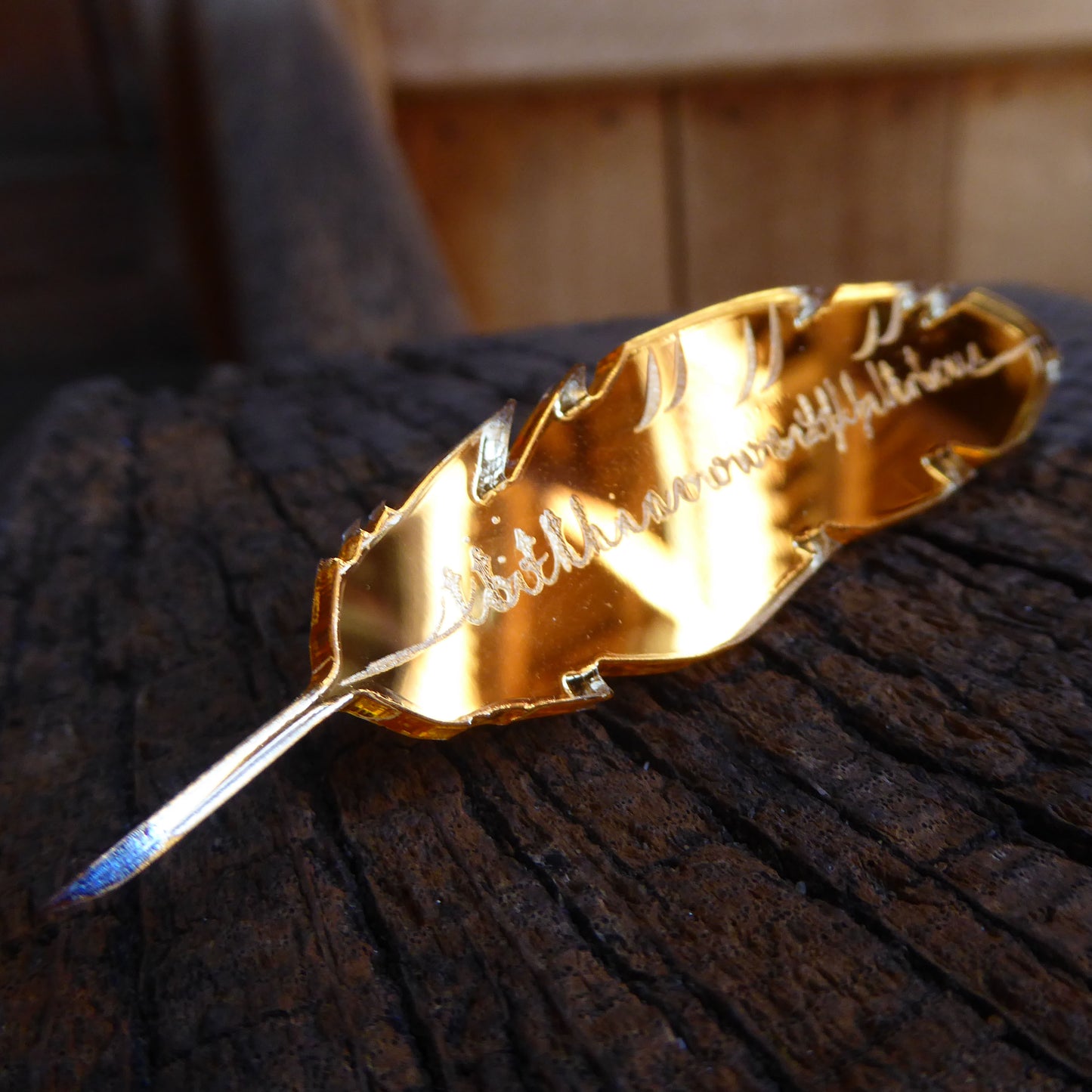 Gold mirrored acrylic brooch in the shape of a feather quill, engraved with a quote from Hamlet