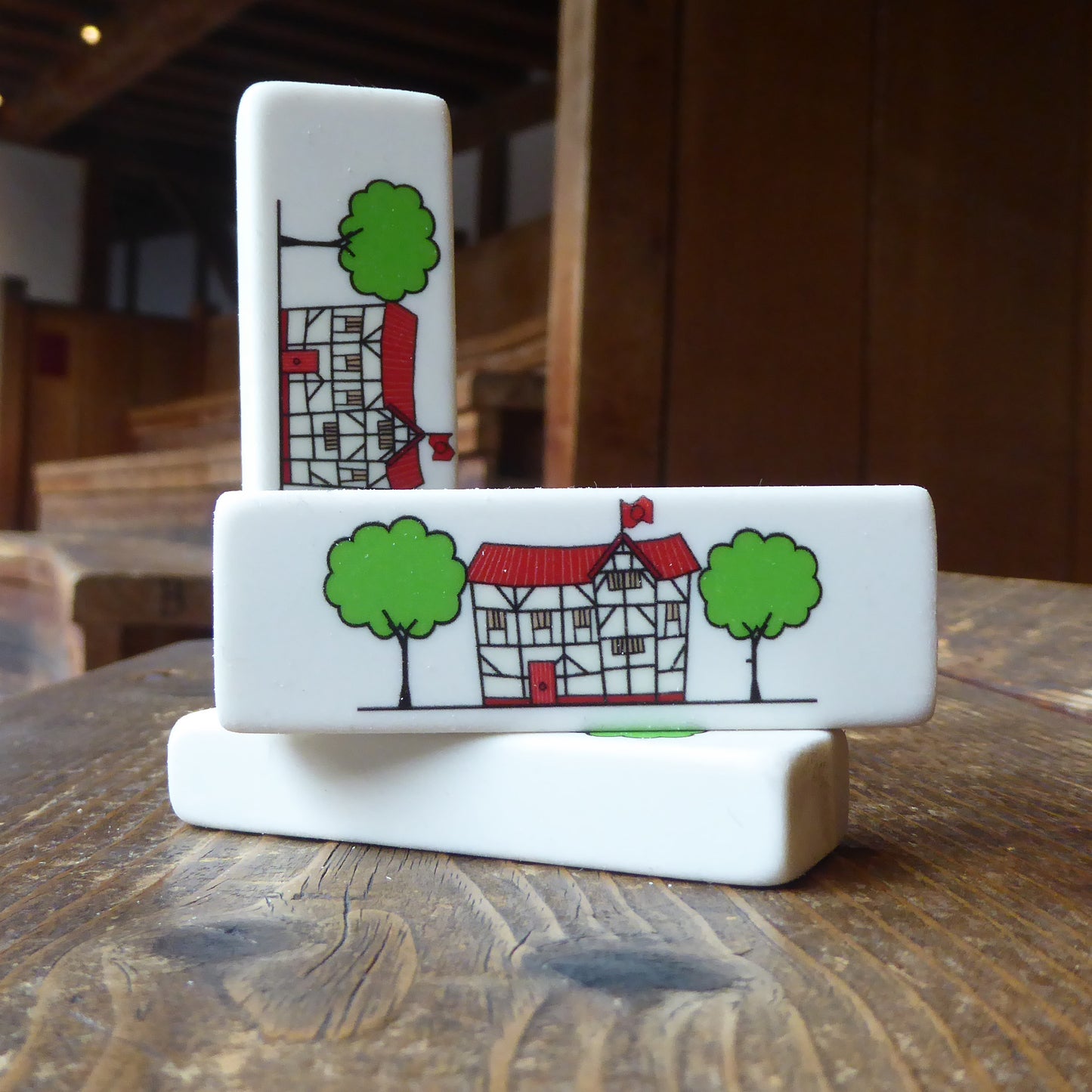 
                  
                    Rectangular white eraser with a print of an illustration of the Globe Theatre in black outline. The theatre also has a red roof and door and is flanked by two green trees. 
                  
                