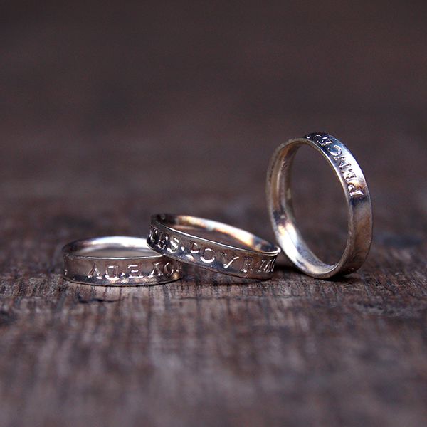 Three silver rings with engravings, sitting on wooden stage