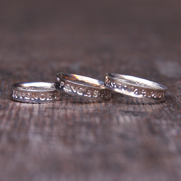 
                      
                        Three silver rings with engravings, sitting on wooden stage
                      
                    