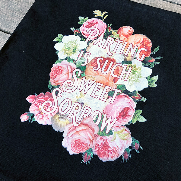 Square black cotton cushion cover with an image celebrating Shakespeare play, Romeo & Juliet. A photographic background of cream, pink and peach roses, with a quote from the play, "parting is such sweet sorrow" in light pink fancy letters.