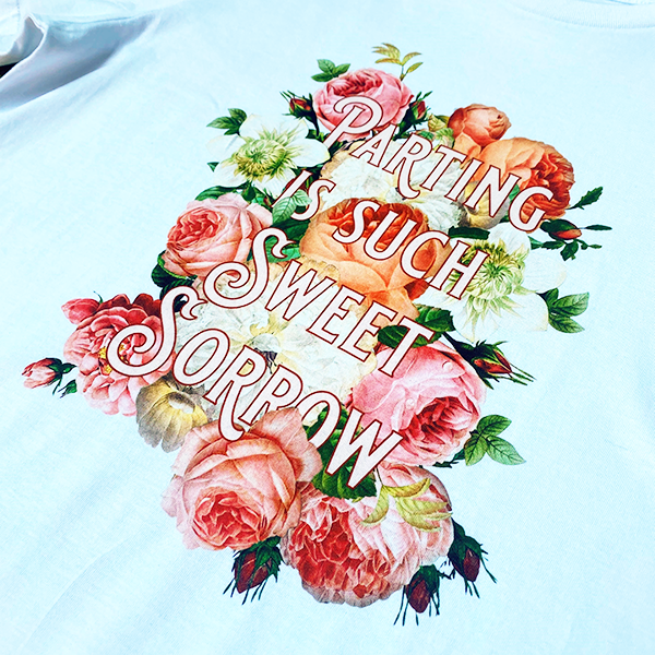 
                  
                    White cotton round-necked, short-sleeved t-shirt with a print celebrating Shakespeare play, Romeo & Juliet. A bed of summer flowers in pinks, peaches and creams frames a quote from the play, "parting is such sweet sorrow" rendered in fancy lettering
                  
                