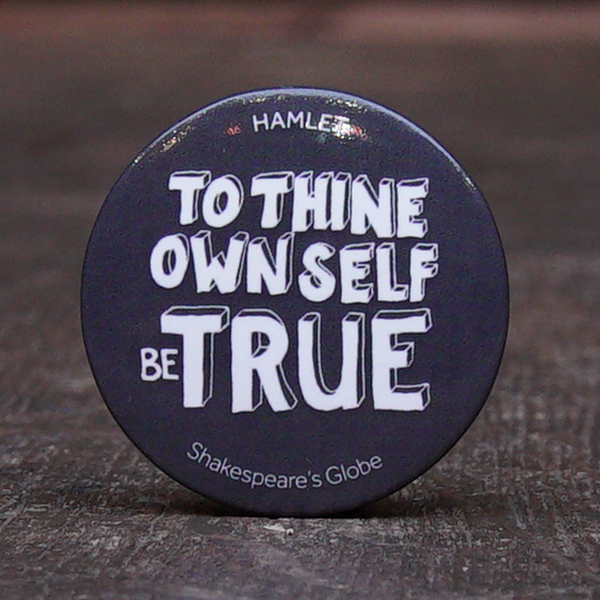 38 mm diametre grey button badge with a quote from Shakespeare play, Hamlet (to thine own self be true) printed in white, hand-drawn, capital letters.