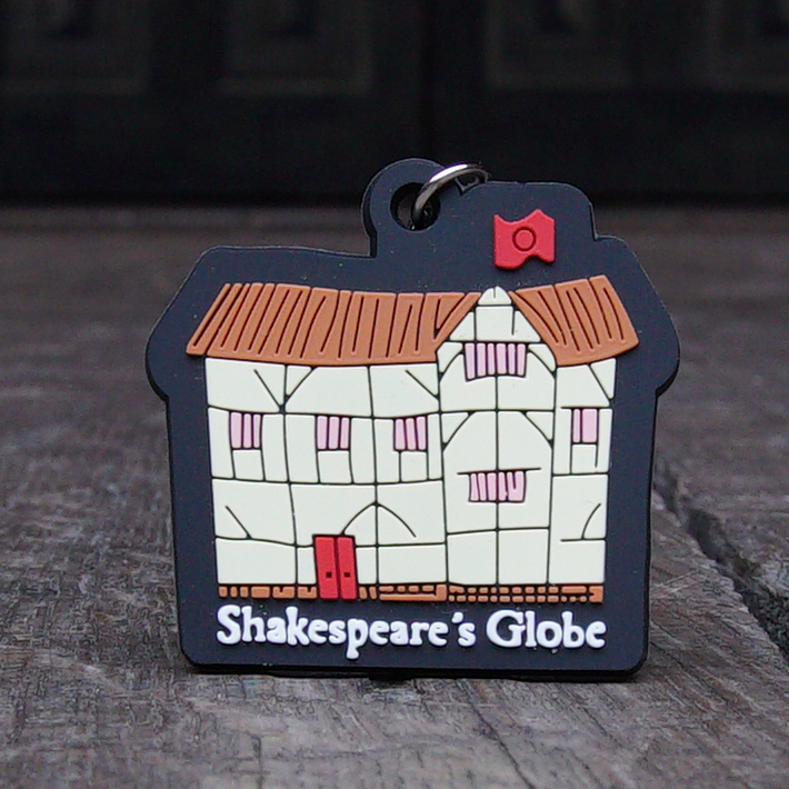PVC key chain with a raised cartoon image of the Globe Theatre. The walls of the theatre are cream with the black frame showing, the roof is brown and the door and flag, red
