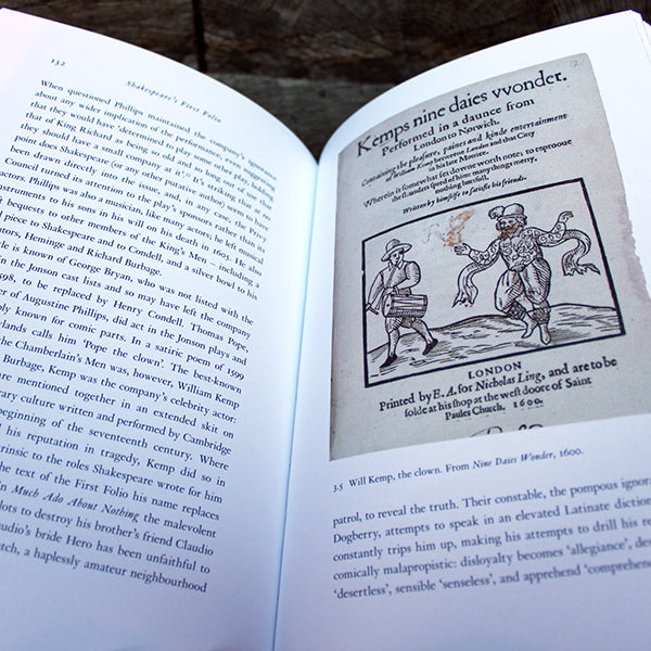 
                  
                    Open hardback book with lines of text on white pages and historical image depicting theatre production
                  
                
