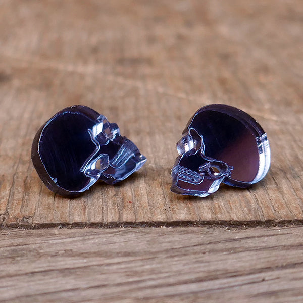 Stud earrings in the shape of a human skull in profile. Made from grey Perspex acrylic with a mirror finish.
