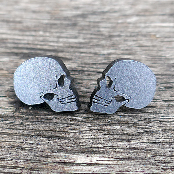 
                  
                    Stud earrings in the shape of a human skull in profile. Made from grey Perspex acrylic with a glitter finish.
                  
                