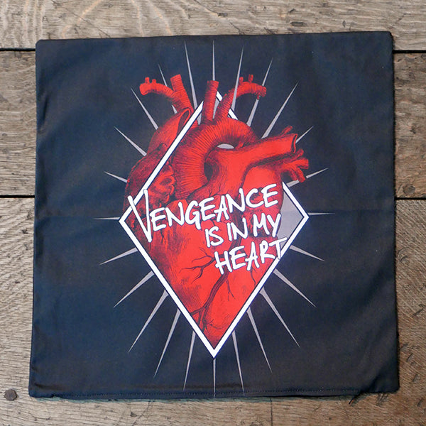 Square, black cotton cushion cover printed with an image celebrating Shakespeare play, Titus Andronicus. An bright red anatomical heart sits within a white diamond-shaped frame with gold-coloured rays emanating from it. A quote from the play, "vengeance is in my heart" is printed over the heart in white hand-drawn letters
