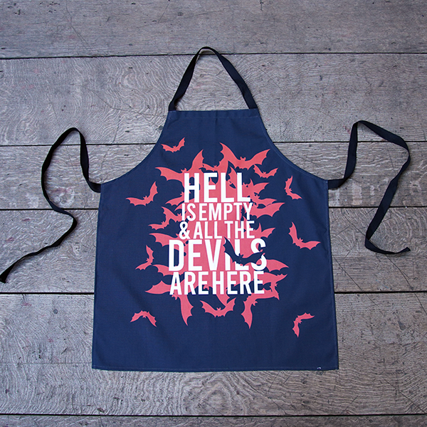 Black cotton apron with black ties and neck loop, printed with a design celebrating Shakespeare play, The Tempest. A cloud of red bats emanate from the centre of the apron. Over the top of the bats is a quote from the play (hell is empty and all the devils are here) in white capital letters.