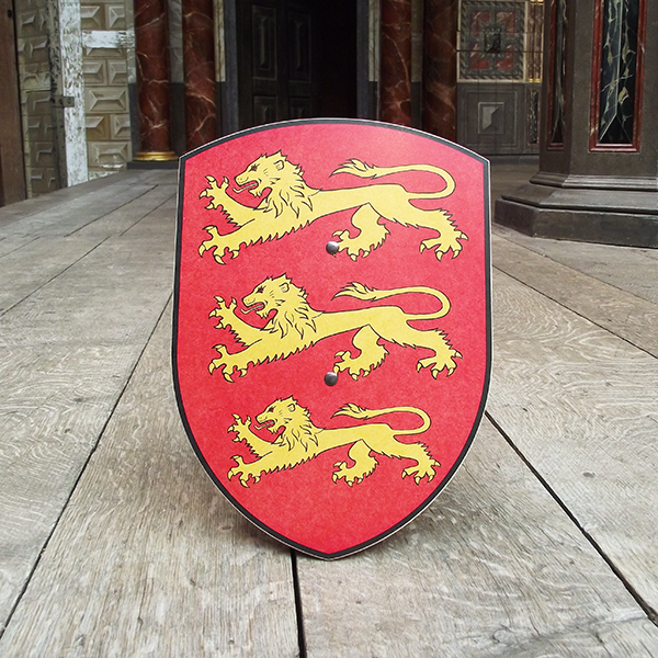 Curved wooden shield with a red background and a golden lion design, along with two lion cubs, positioned on a wooden surface
