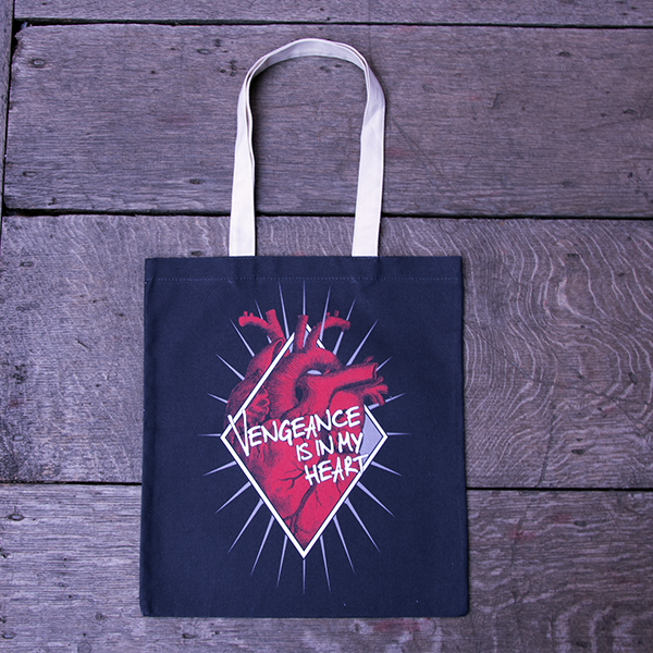 Black cotton bag with natural cotton handles, printed with an image celebrating Shakespeare play, Titus Andronicus. A red anatomical heart is partly enclosed by a white diamond frame. Gold rays emanate from behind the frame. Across the front of the image is a quote from the play (vengeance is in my heart) in white lettering.