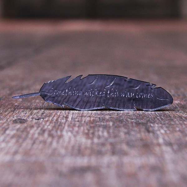 Black, mirrored acrylic brooch in the shape of a quill, engraved with a quote from Shakespeare play, Macbeth, "something wicked this way comes".
