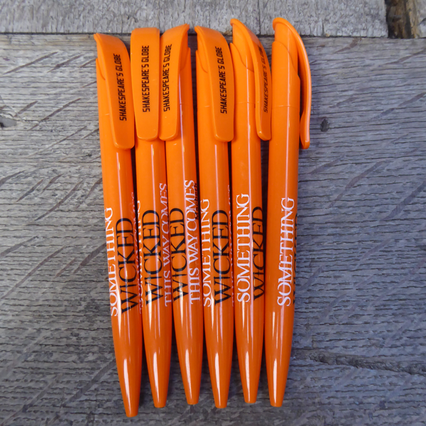 Orange ballpoint pen with a printed quote on the barrel. The quote from Shakespeare play, Macbeth, is printed in black and white capital letters (Something wicked this way comes) The name of the play is printed in black under the quote. The Shakespeare's Globe logo is printed in black on the clip.